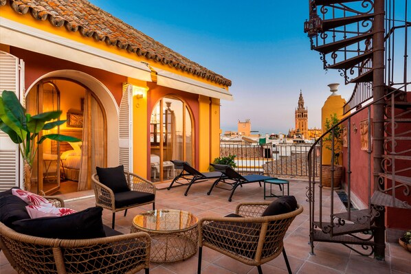 A rooftop terrace with wicker furniture, a glass table, and a view of a historic tower. - Genteel Home San Isidoro Terrace (Seville)