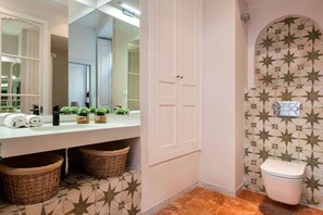 A bathroom with a white vanity, a large mirror, two wicker baskets, a toilet with a star-patterned tile backsplash, and a tiled floor. - Genteel Home San Isidoro Terrace (Seville)
