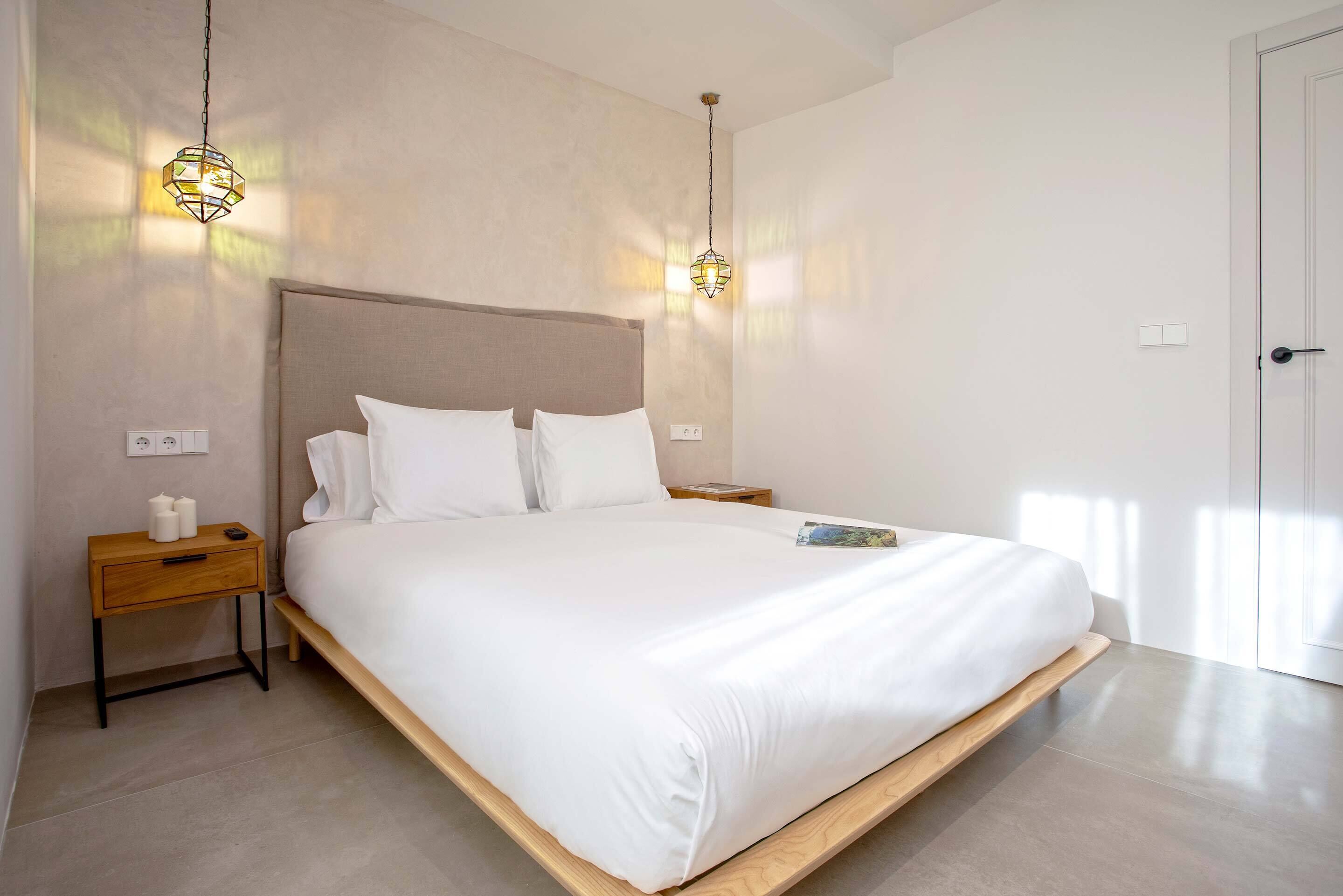 A modern bedroom with a large bed, bedside tables, and pendant lights.