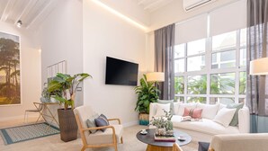 A modern living room with a white sofa, a coffee table, and a TV mounted on the wall. There are potted plants and a large window with curtains. - Genteel Home Plaza del Obispo (Málaga)