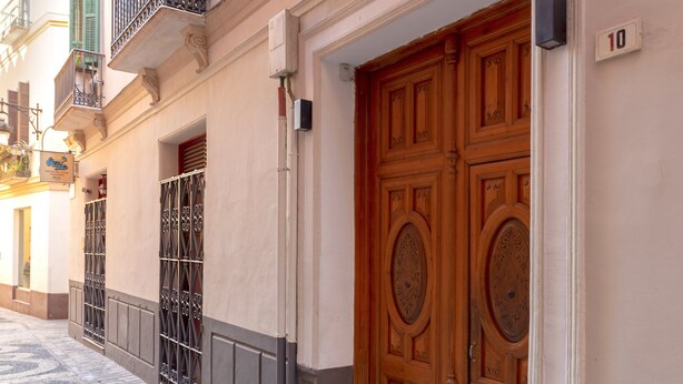 A building with a large wooden double door, a balcony with a wrought iron railing, and a street with cobblestone pavement. - Genteel Home Plaza del Obispo (Málaga)