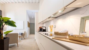 A modern kitchen with a white countertop, a built-in stove, and a large window. There is a plant in a black pot and a chair with a cushion. - Genteel Home Plaza del Obispo (Málaga)