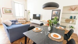 Ein modernes Wohnzimmer mit einer Couch, einem Esstisch für zwei Personen und einem Fernseher.