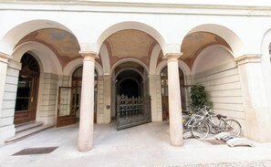 Un edificio con una entrada central enmarcada por tres arcos, un área con reja y bicicletas estacionadas afuera.