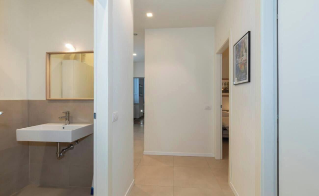 Un couloir étroit, avec une salle de bain sur la gauche, comprenant un lavabo et un miroir.