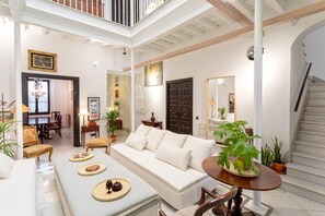 Ein geräumiges Wohnzimmer mit einem weißen Sofa, einem Esstisch mit Pflanze und einer Treppe, die in eine obere Etage führt.
