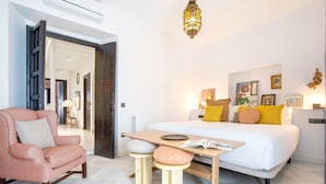 Een moderne slaapkamer met een bed, een houten tafel, een roze fauteuil en een klein krukje.