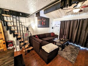 Una sala de estar acogedora con un sofá seccional marrón, una mesa de centro y una escalera con barandillas negras.