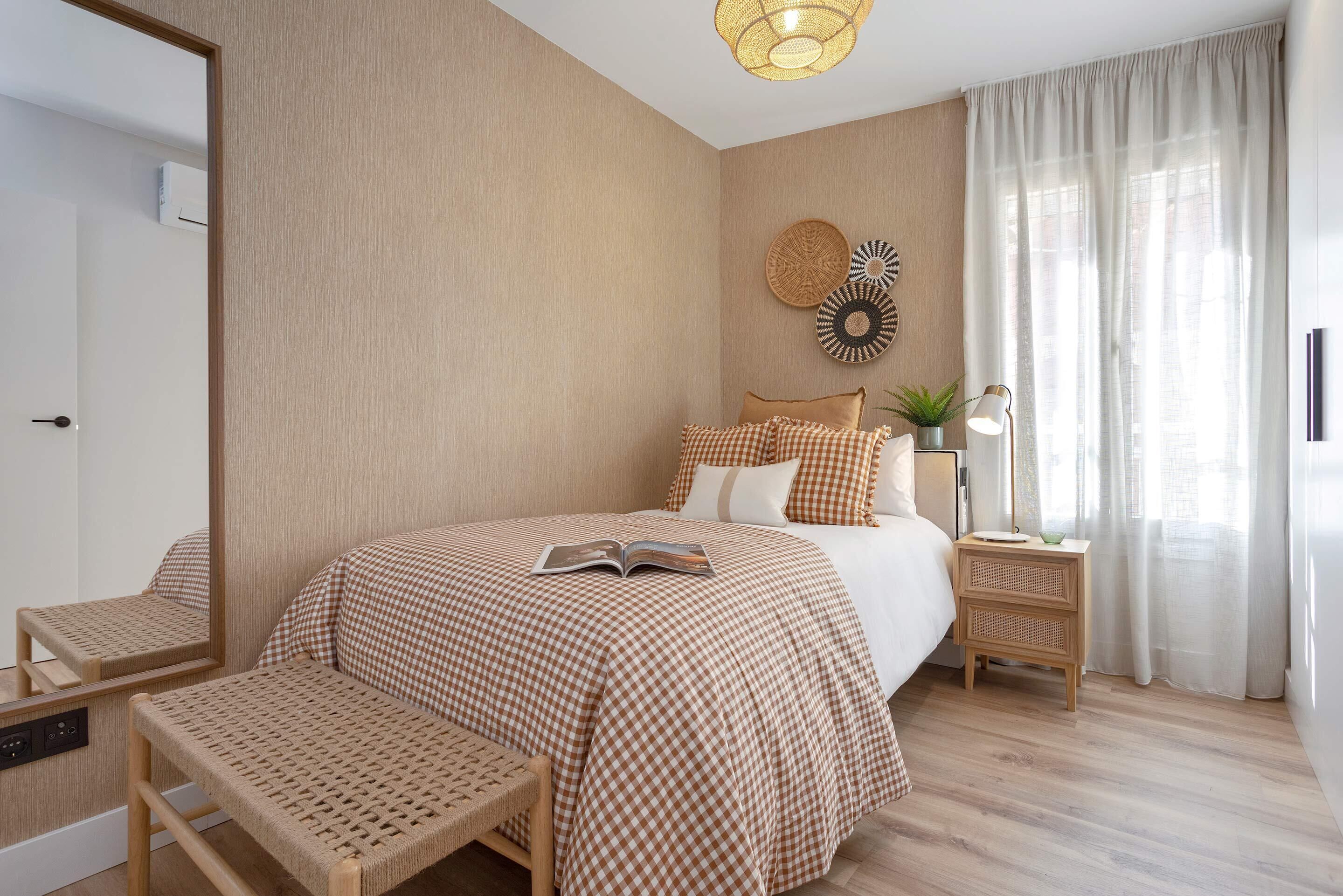A bedroom with a large bed, a bedside table with a lamp, a bench, and a wall-mounted mirror.