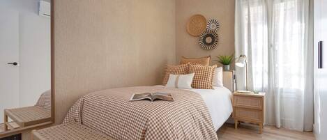 A bedroom with a large bed, a bedside table with a lamp, a bench, and a wall-mounted mirror.