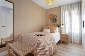 A bedroom with a large bed, a bedside table with a lamp, a bench, and a wall-mounted mirror. - Genteel Home Hermosilla (Málaga)