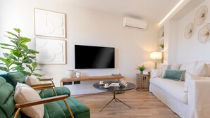 Un salon moderne avec un canapé vert, un canapé blanc, une table basse ronde et un téléviseur à écran plat fixé au mur.