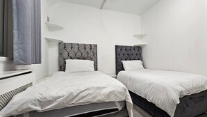 A bedroom with two beds, each with a tufted headboard, white bedding, and a small bedside table. - Spacious & Modern 2-bed House in Dagenham (Dagenham)