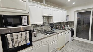 A modern kitchen with white cabinetry, a built-in microwave, a gas stove, and a dishwasher. - Spacious & Modern 2-bed House in Dagenham (Dagenham)