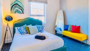 Een hotelkamer met een bed, een slaapbank, een surfboard en een schilderij aan de muur.
