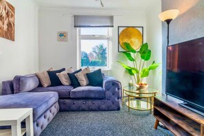 A living room with a purple sofa, a glass coffee table, a TV, and a large plant. - Rayleigh Retreat-spacious Family 3 Bed Apartment (Rayleigh)