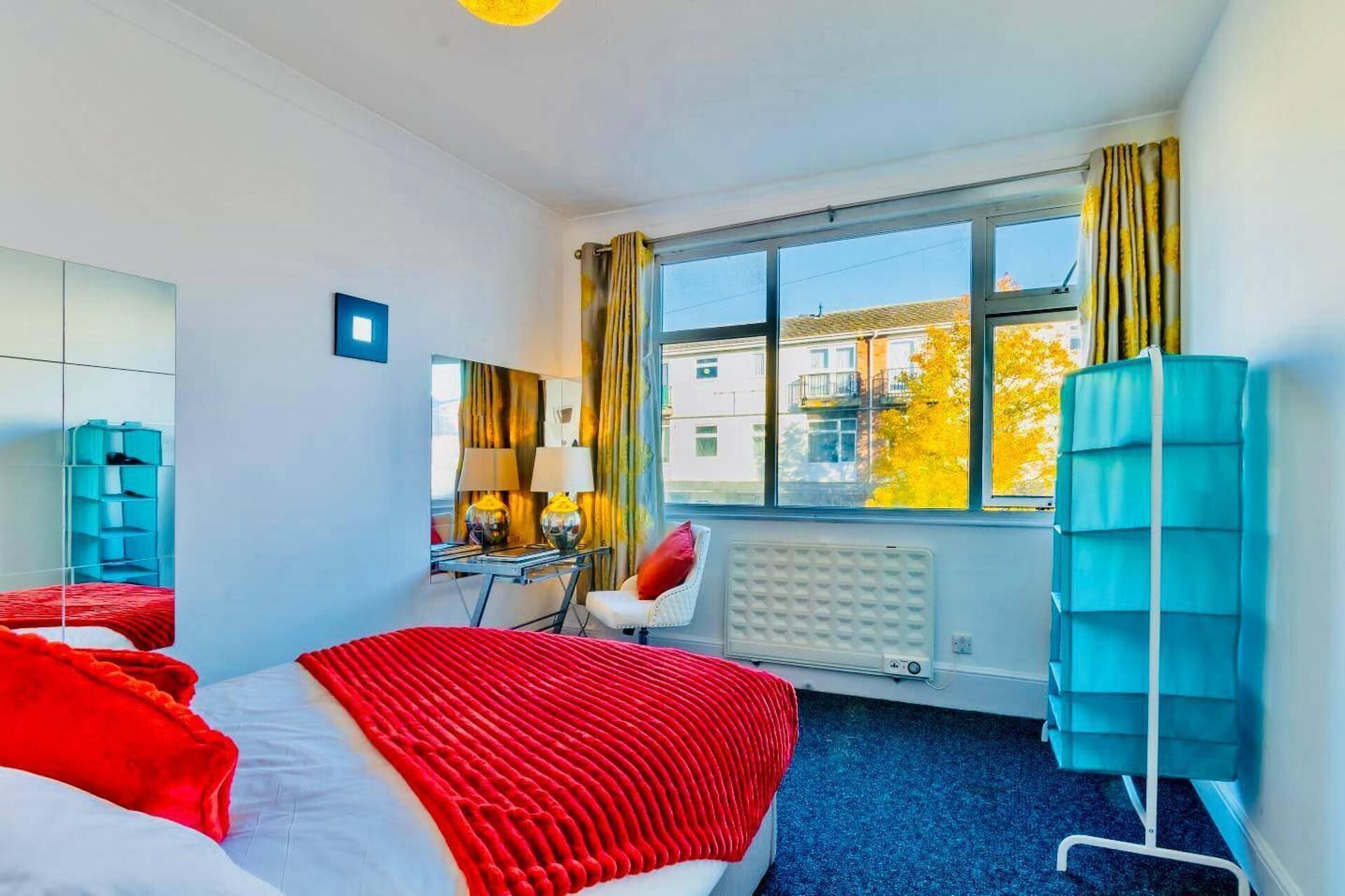 Ett hotellrum med en säng, ett skrivbord, en stol, ett element och ett fönster med gardiner.
