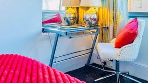 Een hotelkamer met een bed, een bureau met twee lampen, een stoel en een raam met gordijnen.