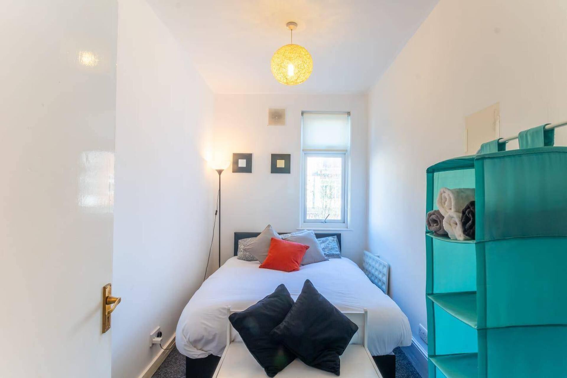 Ein Schlafzimmer mit einem Bett, einer grünen Kommode, einem Fenster und einer Stehlampe.