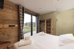 A bedroom with a large bed, a wooden wardrobe, and a view of the outdoors.