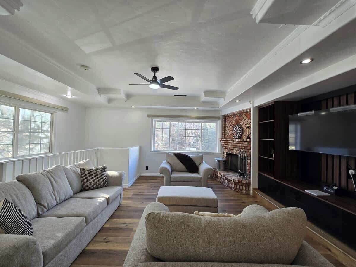 Uma sala de estar ampla com lareira, uma televisão de tela grande e um ventilador de teto.