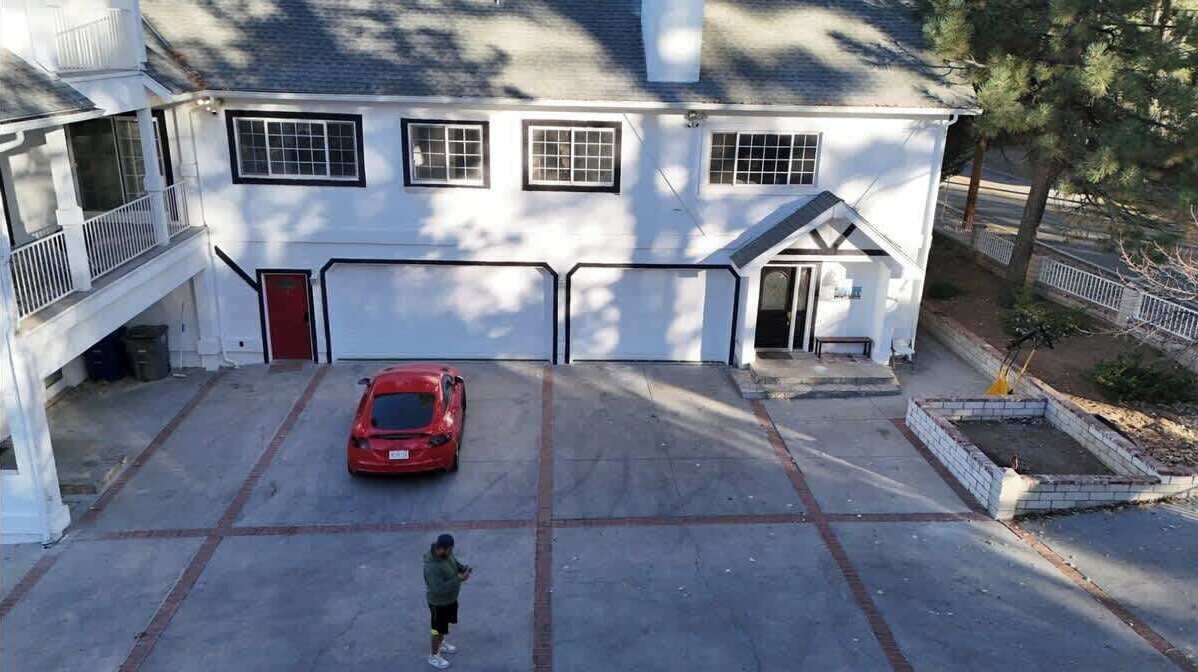 Et hvidt toetagershus med en rød bil parkeret i indkørslen, et barn foran, og en hegnet have.