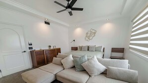 Een moderne slaapkamer met een groot bed, een bank, een dressoir en een plafondventilator.