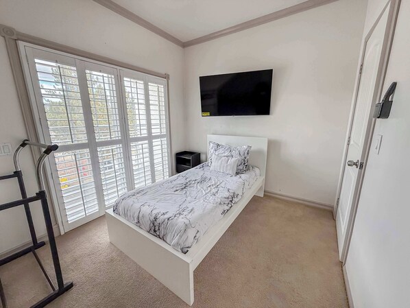 A bedroom with a bed, a TV, a window with blinds, and a door.