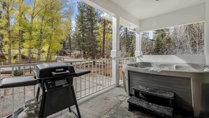 Een terras buiten met een barbecue, een jacuzzi en uitzicht op bomen en een straat.