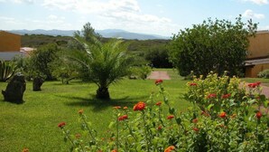 A well-maintained garden with a palm tree, red flowers, and a clear view of distant mountains. - Hotiday Golfo Aranci (Golfo Aranci)