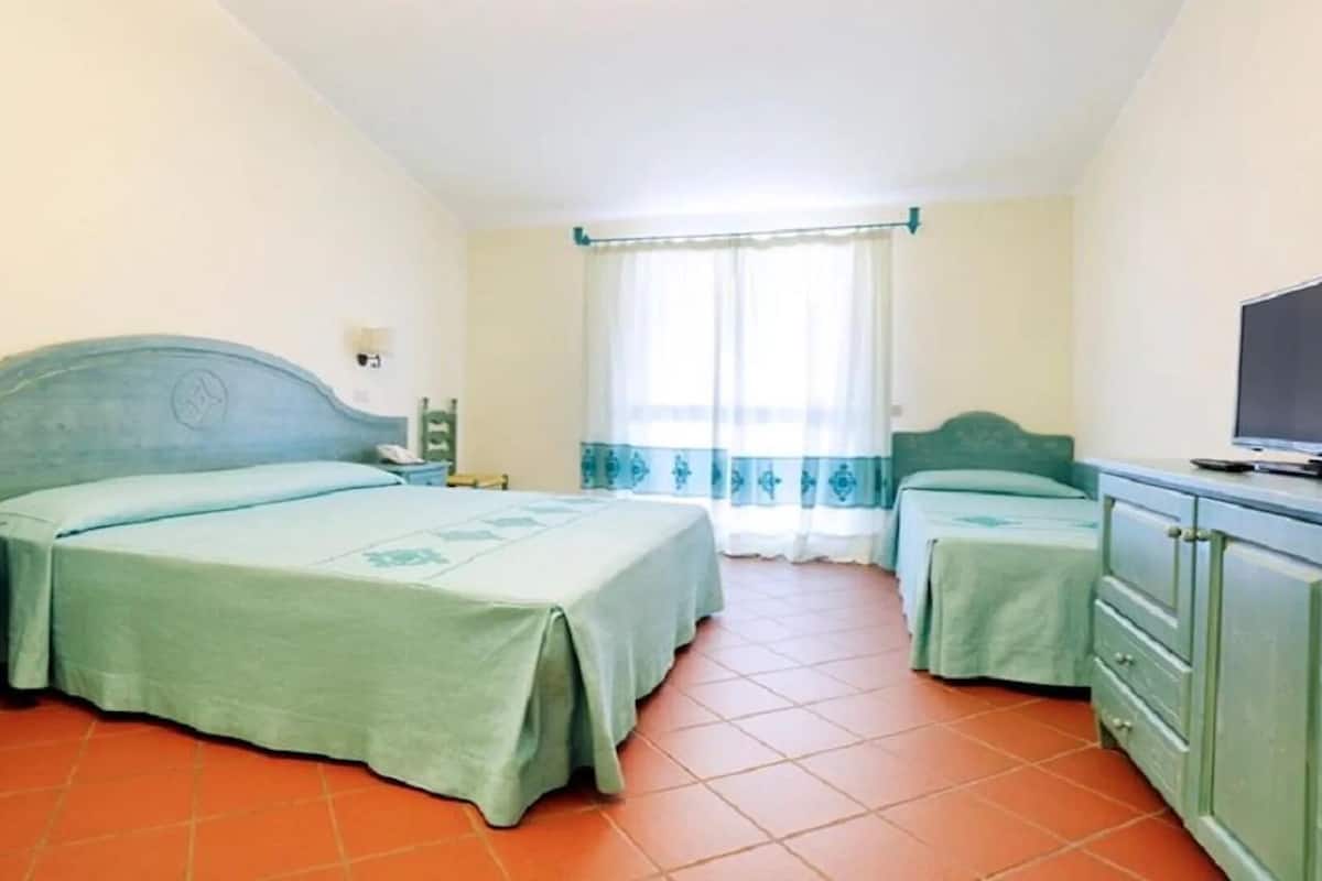 A hotel room with two beds, a TV, a desk, and a window with curtains.