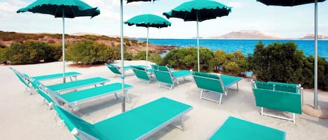 A beachside lounge area with multiple green lounge chairs and umbrellas, overlooking a coastal landscape.