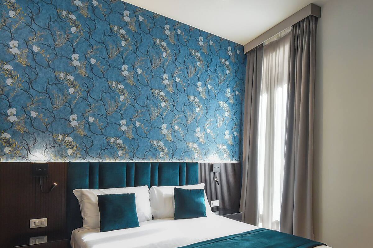 A large bed with a teal bedspread, a dark headboard, and a wall with a floral pattern.