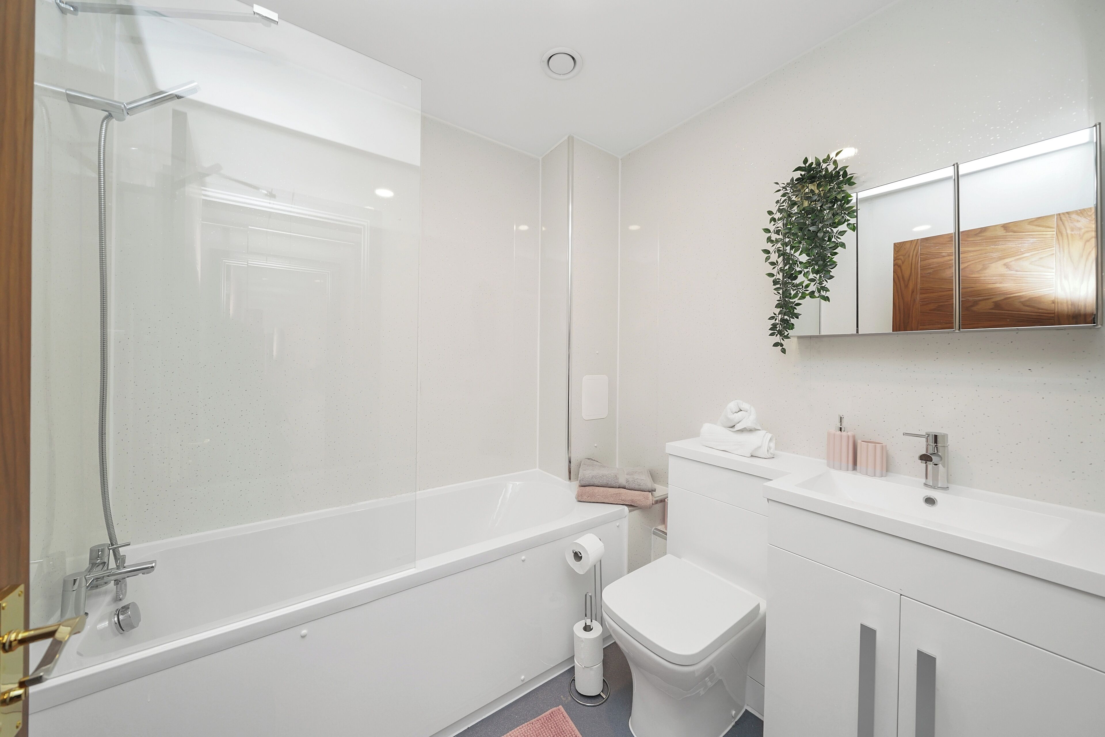 Un baño moderno con ducha acristalada, inodoro y lavamanos con espejo.