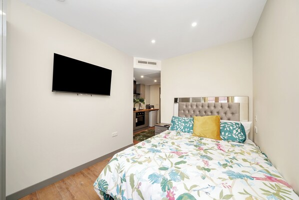 A bedroom with a bed, a television mounted on the wall, and a view into the kitchen area. - Hotel Apartment in Ilford (Ilford)