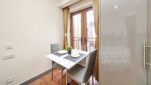 A small dining area with a table set for two, a potted plant, and a view of a balcony. - Hotel Apartment in Ilford (Ilford)
