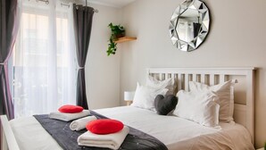 A neatly made bed with white and red pillows, a black headboard, and a round mirror on the wall. - 123home- Suite & spa XL (Montevrain)