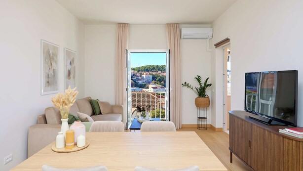 Una sala de estar moderna con comedor, televisor y balcón con vista a la ciudad.