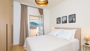 Habitación de hotel con una cama, una mesita de noche, una lámpara, un ventanal con cortinas y tres cuadros en la pared.