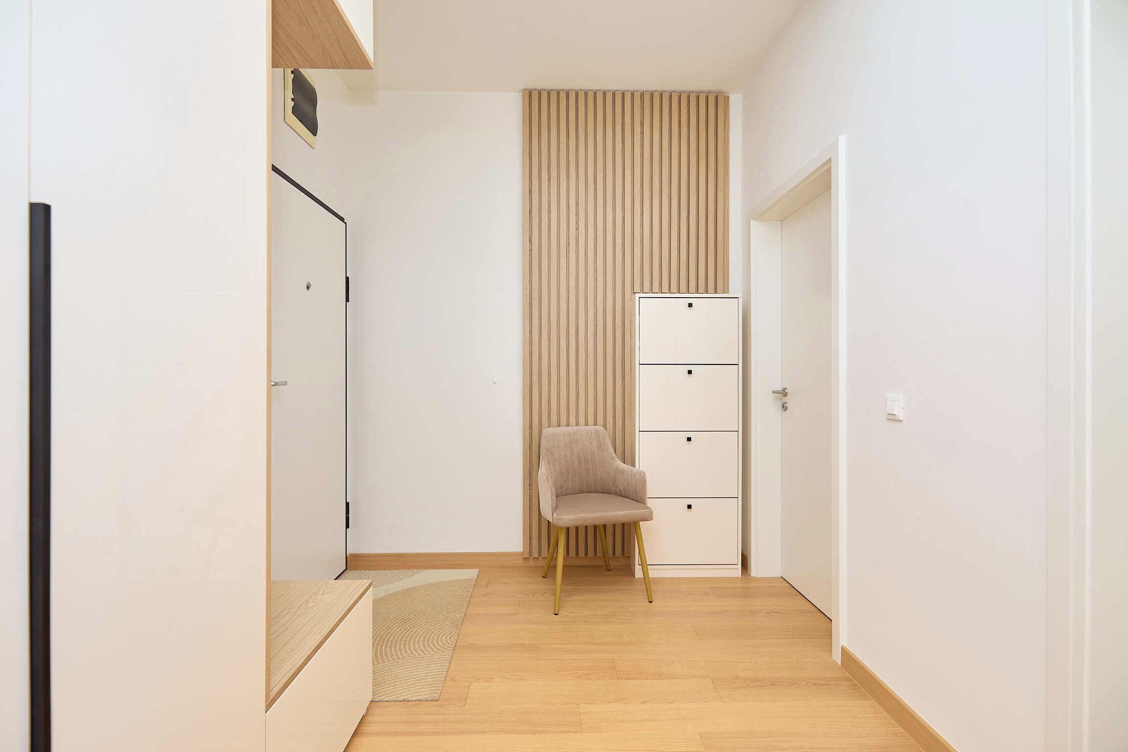 A hallway with a wooden floor, a beige chair, and a white wardrobe with drawers.