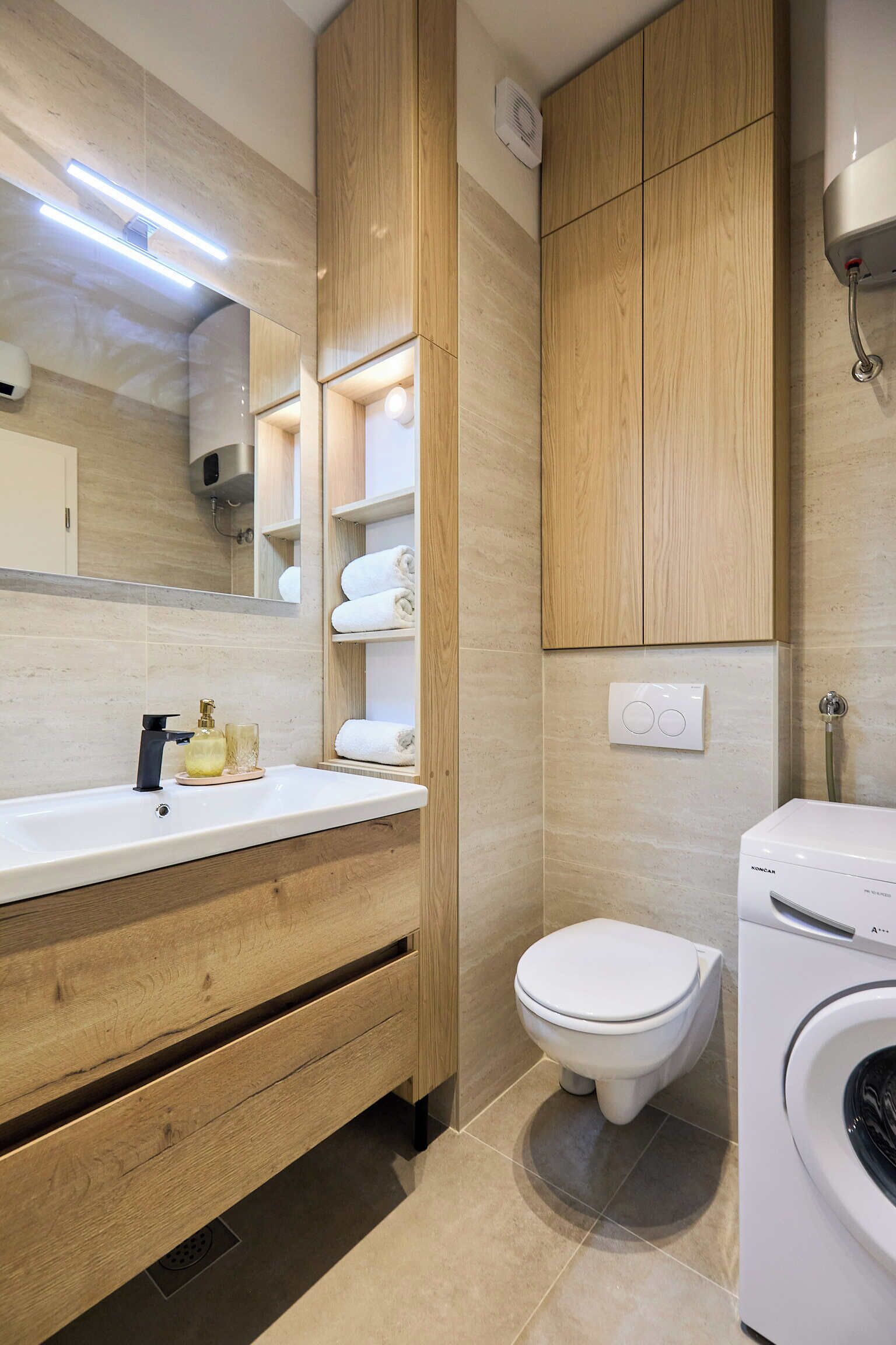 Ein modernes Badezimmer mit einem Holzlagerfläschchen, einem weißen Waschbecken, einem Spiegel, einer Toilette und einer Waschmaschine.