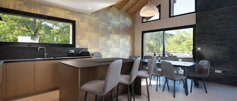 Una cucina moderna con isola centrale, zona pranzo con sedie, ampie finestre e vista su spazi verdi.
