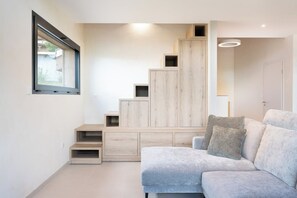 A modern living room with a built-in staircase, a sofa, and a window.