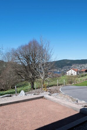 A rural landscape with a clear sky, a dirt path, a leafless tree, and a white building in the background.
