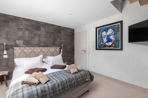 A modern bedroom with a large bed, a headboard, a flat-screen TV, and a painting on the wall.