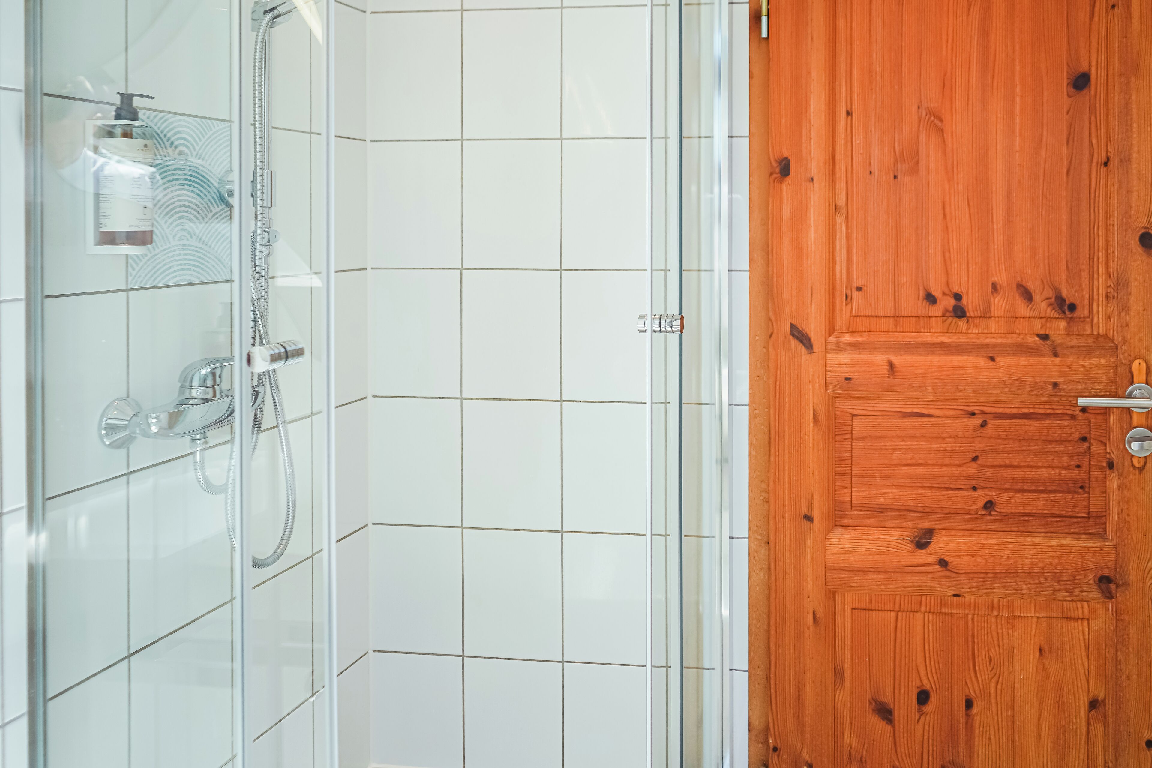Un baño con cabina de ducha de vidrio, puerta de madera y paredes con azulejos.