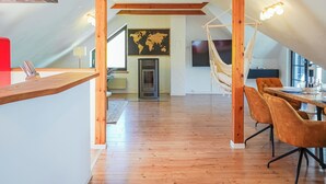 A modern loft-style room with exposed wooden beams, a dining area with orange chairs, and a world map on the wall.