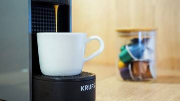 Een witte koffiekop op een Krups koffieapparaat, met een pot koffiepads op de achtergrond.