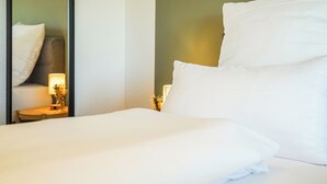 A neatly made bed with white linens, a bedside lamp, and a small table with a vase of flowers.