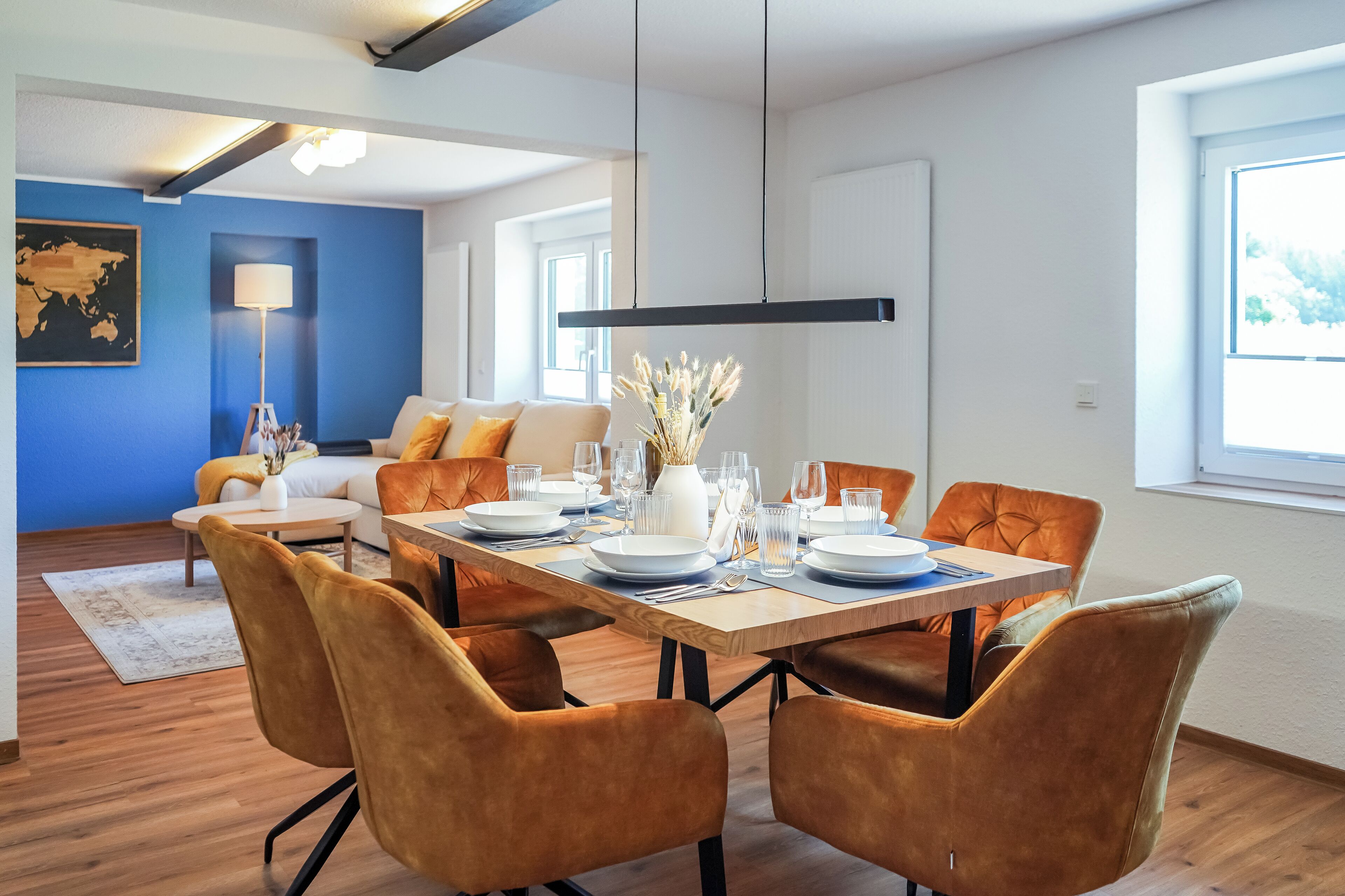 A modern dining area with a wooden table set for six, surrounded by orange chairs.
